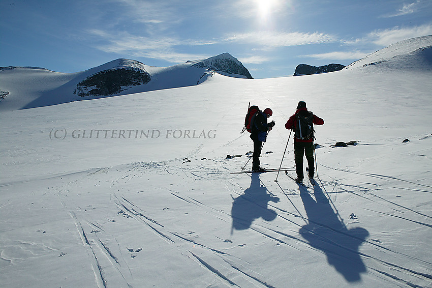 To skiløpere i silhuett ved kanten av Styggebrean med Galdhøpiggen i bakgrunnen.