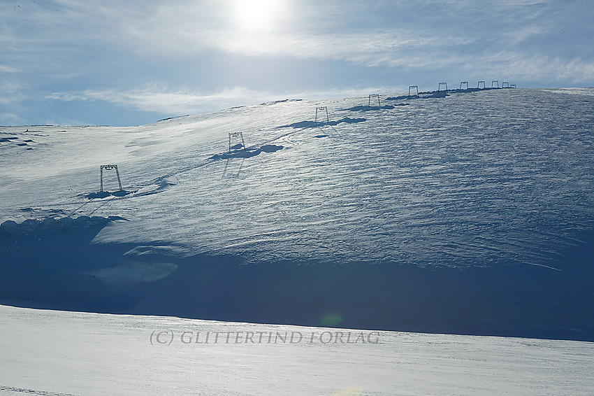 Juvvatnet med den vinterfrosne Vesljuvbrean som velter ut mot vannet og skitrekket som er reist oppå breen.