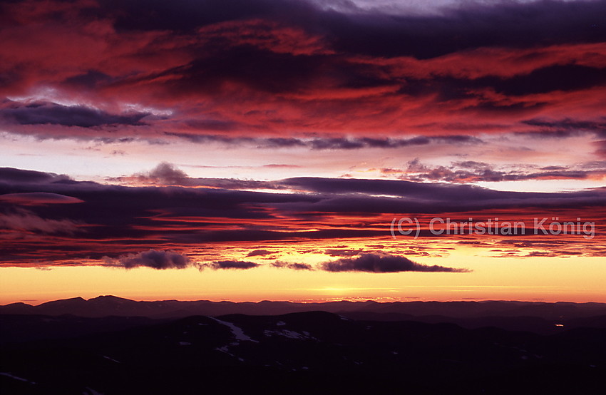 View from the top of Glittertinden facing a northern direction waiting for sunrise. Sun is hiding only a bit under the horizon already illuminating the clouds.