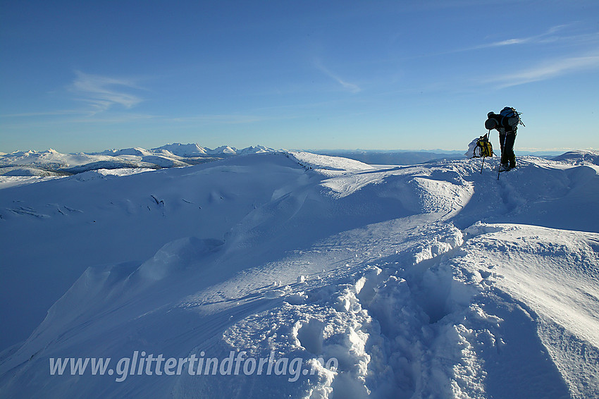 På Søre Tverrådalskyrkja med Steinkollen og Hurrungane i bakgrunnen. Det har blitt mange timer med vassing i dyp snø og kreftene begynner å sive ut. Da er det godt å henge litt på stavene.