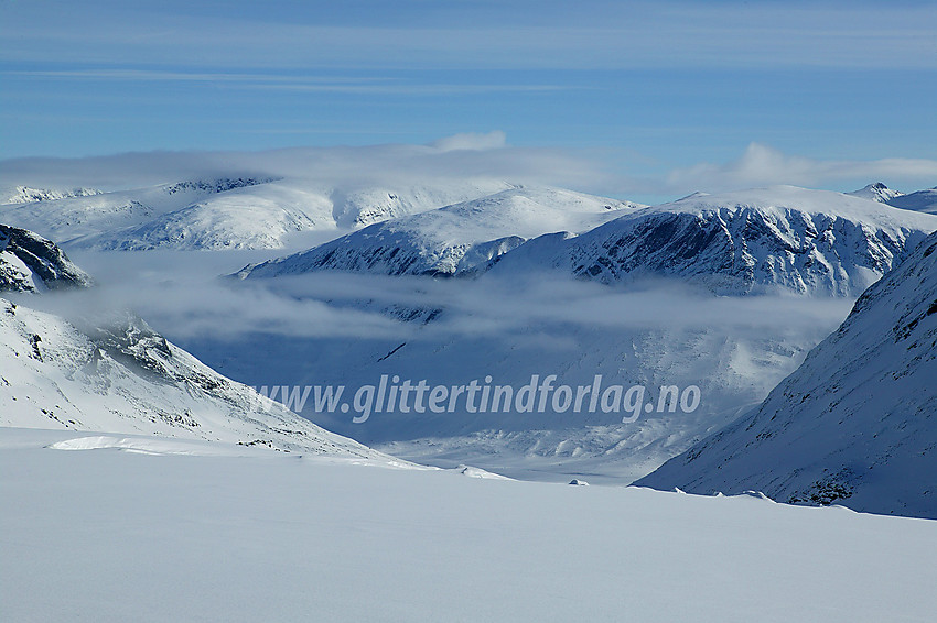 Morgenstund utenfor snøhula på Tverråbrean innunder Nørdre Bukkeholstinden med utsikt mot Visdalen med Spiterhøe (2033 moh) til høyre og Skauthøe (1933 moh) til venstre. Til venstre bak sistnevnte ruver Glittertinden med toppen i tåka.