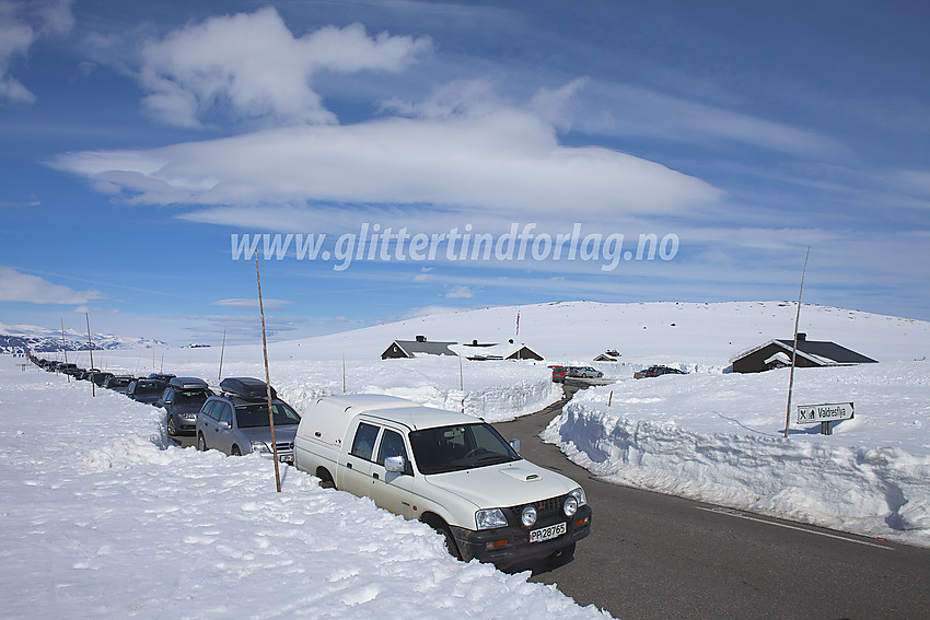 Lang rekke av biler parkert langs toppen på Valdresflye. I bakgrunnen det tidligere vandrerhjemmet.