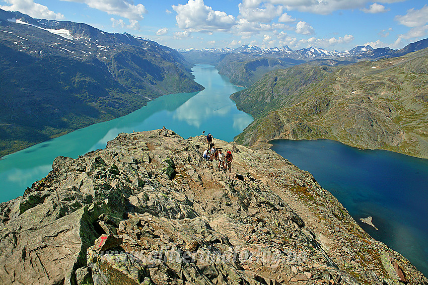 Fjellvandrere på vei opp Besseggen med det klassiske panoramaet med bregrønne Gjende til venstre og det langt mer sortblå Bessvatnet til høyre.