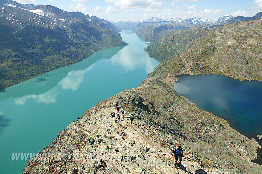 Fjellvandrere på vei opp Besseggen en flott sommerdag. Til venstre det bregrønne Gjende og til høyre det dypblå Bessvatnet. Hvis du kan se Gjendebåtene ute på Gjende i form av to små prikker, får du litt inntrykk av dimensjonene på landskapet.