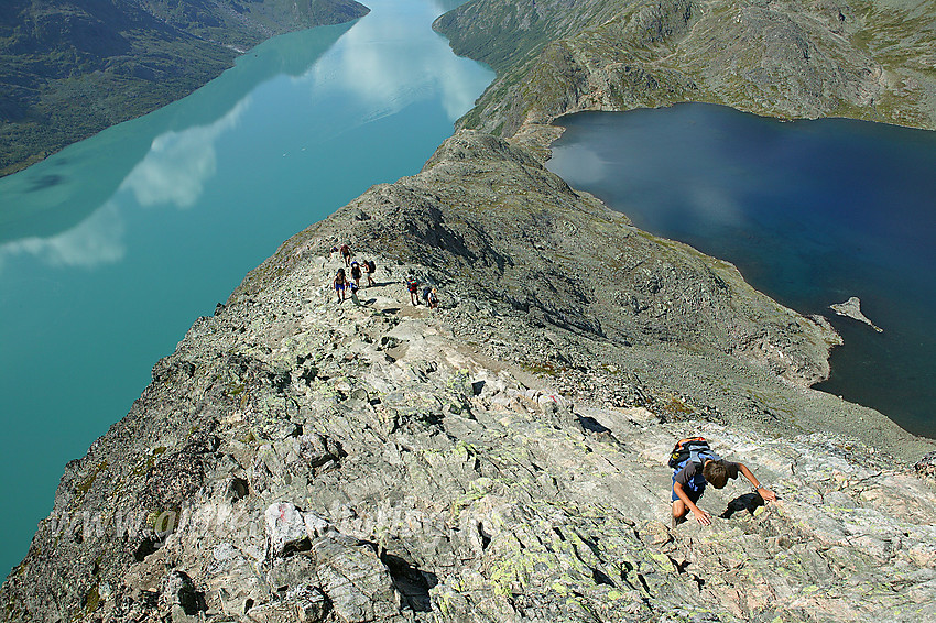 Fjellvandrere på vei opp Besseggen med Gjende og Bessvatnet i bakgrunnen. Besseggen har i hovedsak to små klyvepassasjer. Den øverste av disse ses helt i forgrunnen, mens den andre er litt lenger nede bak gruppa på bildet.