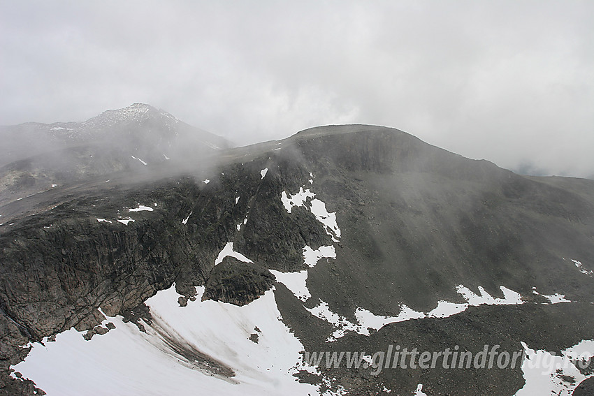 Utsikt fra Skarvflyløyftbrean mot Tjønnholsoksle (2145 moh) og Tjønnholstinden (2329 moh). En heller grå dag med tåkeskyer rundt toppene.