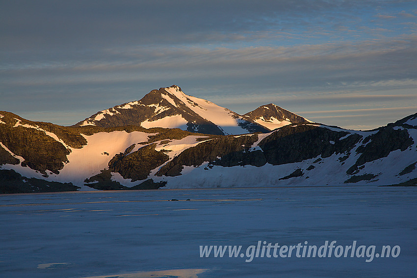 Ved det islagt Hinnåtetjønne en sommermorgen med Skarddalseggje (2159 moh) og Skarddalstinden (2100 moh) i morgensol i bakgrunnen.