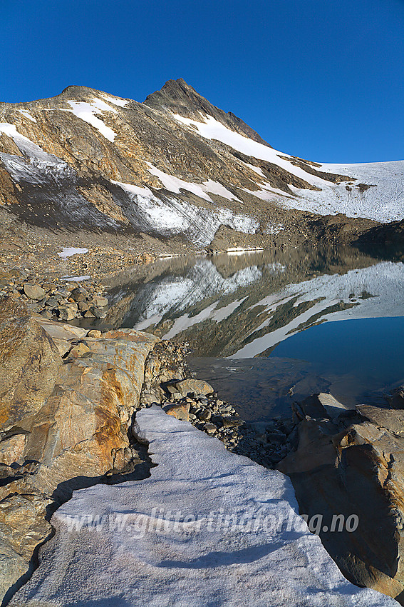 Ved et lite brevann som har smeltet frem ved fronten av Uranosbreen (på litt eldre kart er det tegnet inn isbre her). I bakgrunnen ruver sørryggen på Uranostinden med Uranostinden S2 (2048 moh) som det spisse punktet øverst på eggen. Selve Uranostinden ses såvidt i bakgrunnen.