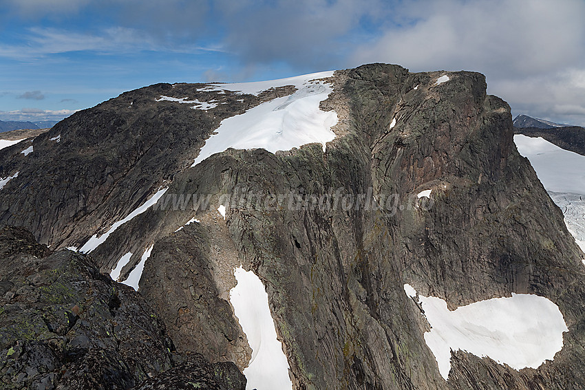 På ryggen øst for Slettmarkpiggen med utsikt bort til Slettmarkhøe (ca. 2190 moh). Nedenfor den store snøfonna på Slettmarkhøe er det et brattere klippeparti. Det kan se ganske guffent ut på avstand, men det løser seg greit opp og byr ikke på annet en moderat klyving.