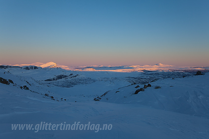 På vei ned fra Mugnetinden en januarettermiddag mens sola går ned. I bakgrunnen ses bl.a. Bitihorn (1607 moh) og Skaget (1686 moh).