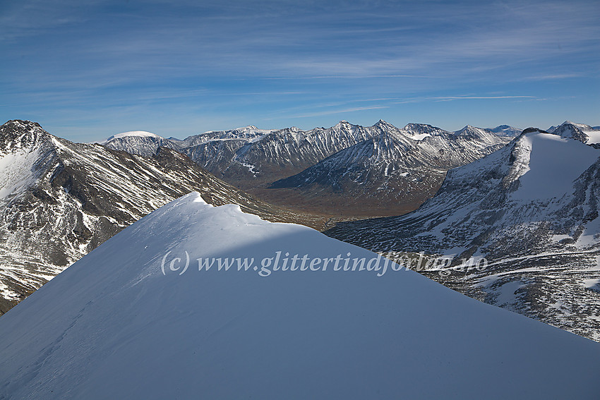 På snøkammen like øst for Midtre Tverrbottinden Nord. Til venstre ses Store Bukkeholstinden (2213 moh.) og til høyre Tverrbytthornet (2102 moh.). Lenger bak bl.a. Urdadalsryggen, Hellstuguryggen, Memurutinder og Leirhøe.