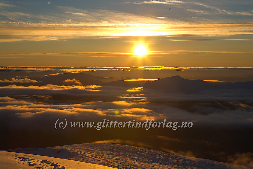 Fra Glittertinden mot morgensola i øst-sørøst. Tåkeskyer svever over Veodalen og glinser i sola, mens silhuetten til Stornubben (2174 moh.) dominerer midt i bildet.