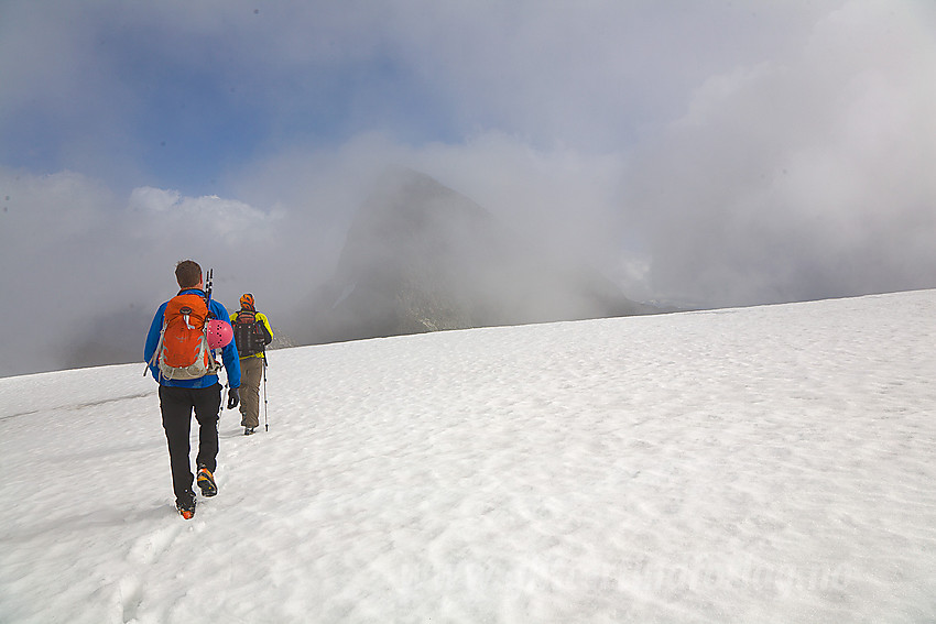 Fjellvandere på vei over Stølsnosi med kurs mot Stølsnostinden (2174 moh) som kan skimtes gjennom tåkeskyene.