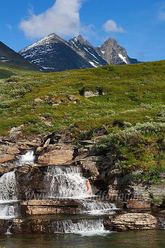 Ved broa over Helgedalselvi like før Turtagrø når man kommer fra Berdalsbandet. Her er en flott liten foss med tilhørende badekulper. I bakgrunnen troner Skagastølstindane som vakker kulisse.