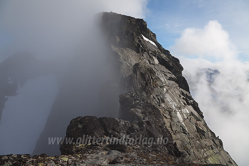 Fra sørligste Austanbotintinden mot den vesle pinakkelen (går nesten i ett med bakgrunnen) og Søre Austanbotntinden (2103 moh). Klamme morgengretne tåkeskyer klamrer seg ennå til fjellsidene mens sola jobber med å gjøre kål på dem.