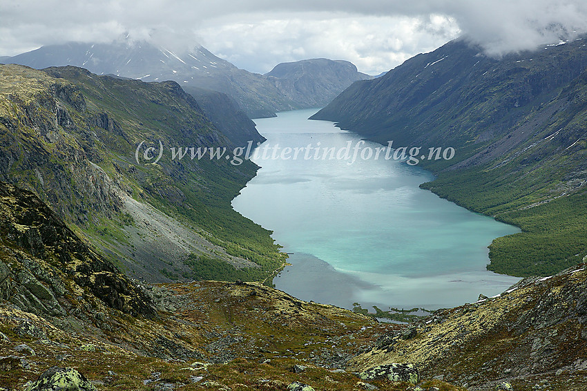 Utsikt østover fra oppunder Gjendetunga (1516 moh.) mot billedskjønne Gjende med Besshøe (delvis i tåke) og Veslfjellet med Besseggen i bakgrunnen. Langt ute på Gjende kan man ane Gjendebåten som jobber seg vestover som en prikk på vannet.