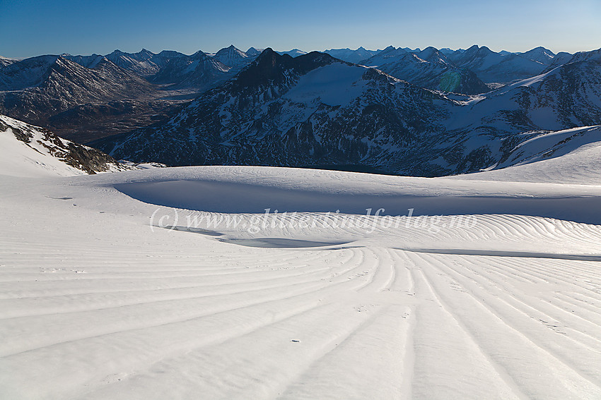 Bjørnskardet er akkurat passert og utsikten åpner seg mot Stetinden og store deler av sentrale Jotunheimen. Legg også merke til de artige stripemønstrene på breen.