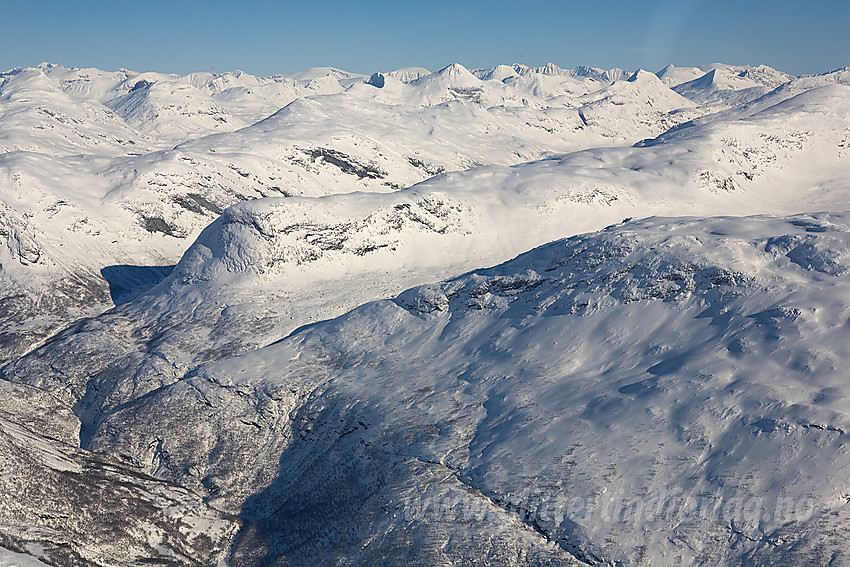 Vi passerer mer enn 1000 meter over bunnen av Utladalen. Skarpe øyer kan legge merke til Skogadalsbøen i venstre bildekant. I bakgrunnen ruver Jotunheimens tinder. Blant de mange toppene er Galdhøpiggen, Glittertinden og Surtninssue å se som de høyeste.