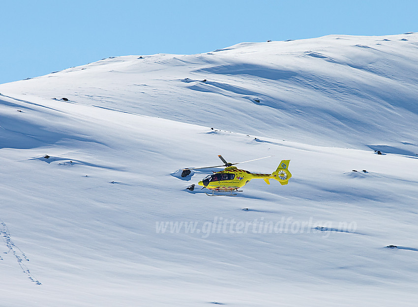 Helikopter i lufta over Øvre Årdalsvatnet ved foten av Slettningsegge.