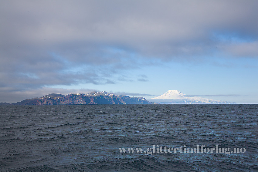 Vi nærmer oss Jan Mayen. Sør Jan i forgrunnen med sine klippekyster og Nord Jan i bakgrunnen med kjempen Beerenberg (2277 moh).