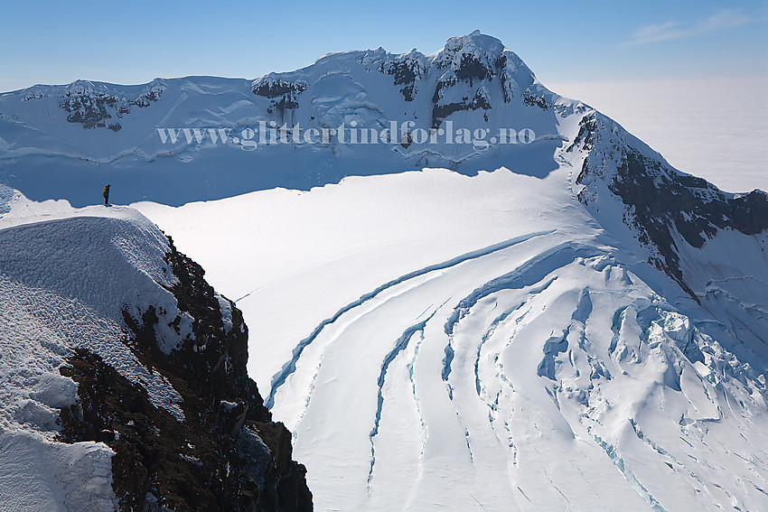 Person ute på et fremspring oppe ved Hakluyttoppen. Det er flott utsikt ned i Sentralkrateret med Weyprechtbreen. På andre siden ses Haakon VII Topp (2277 moh).