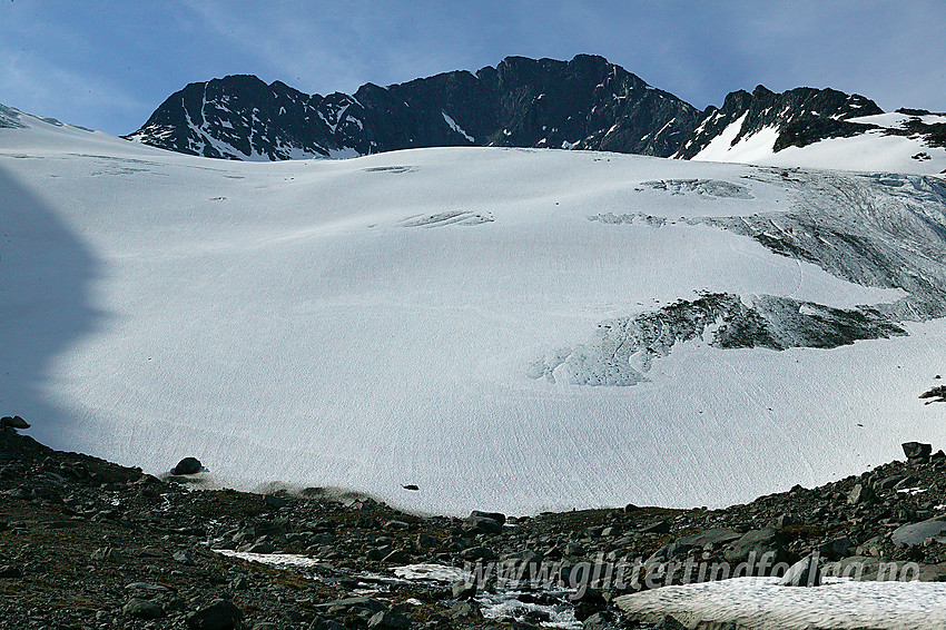 Ved fronten på Visbrean med Visbreatinden (2234 moh) ruvende i bakgrunnen. Til høyre ses nordryggen med to mindre sekundærtopper.