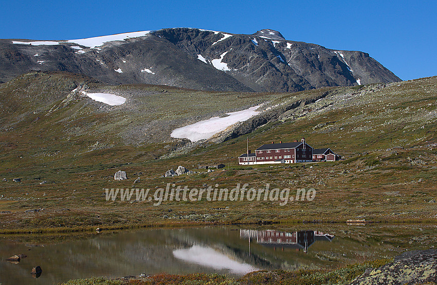 Glitterheim speiler seg i noen småvann nedenfor hytta med Ryggjehøe ruvende ovenfor.