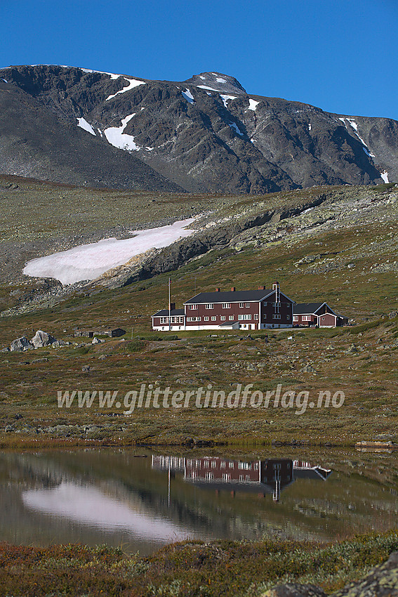 Glitterheim speiler seg i noen småvann nedenfor hytta med Ryggjehøe ruvende ovenfor.