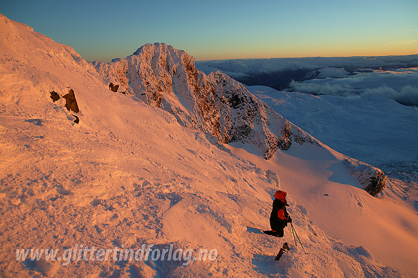 På vei ned fra Vestre Austanbotntinden mens solnedgangen gløder opp fjellsiden. I bakgrunnen bl.a. Søre Austanbotntinden (2103 moh).