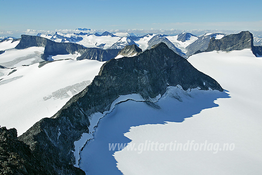 Utsikt fra Galdhøpiggen (2469 moh.) mot Storjuvtinden (2344 moh.) midt i bildet, med Storjuvbrean til høyre,  Svellnosbrean til venstre og Ymelstinden (2304 moh.) rett bak til venstre. Bakenfor ses Bukkehøes (2314 moh.) karakteristiske profil til venstre og Skardstinden (2373 moh.) til høyre. Bak disses ses fjellene vest for Leirdalen, fra høyre mot venstre: Loftet (2170 moh., bak Skardstinden), Veslfjelltinden (2157 moh.), Skagsnebb (2003 moh.) og Bakarste Skagsnebb (2093 moh), Veslbreatinden (2092 moh.) og Storbreahøe (2001 moh.) med Storbreatinden (2018 moh.) så vidt synlig bak denne. Så kommer Storbrean med Store Smørstabbtinden (2208 moh.) lett gjenkjennelig bak og Størebjørn (2222 moh.) til venstre.