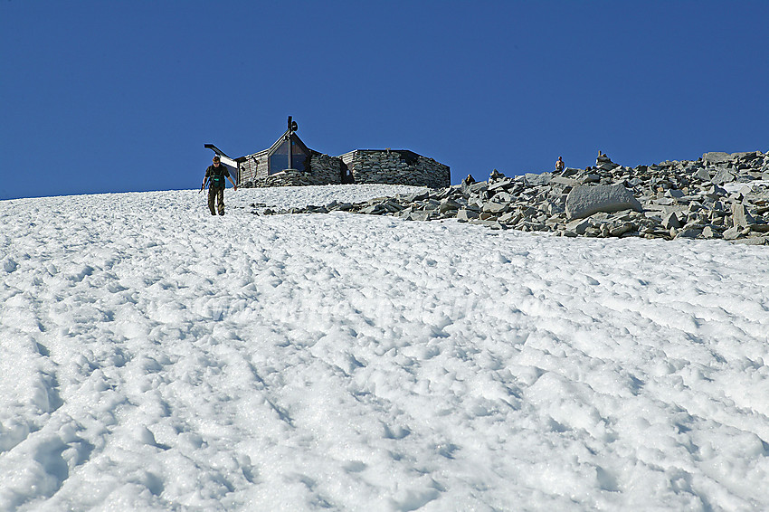 Litt nedenunder toppen på Galdhøpiggen (2469 moh). Den særpregede hytta kneiser mot en knallblå himmel. 