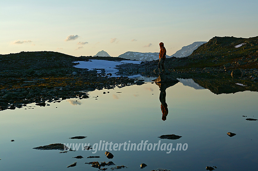 Ved et lite vann ved Utsikten en blikkstille sommerkveld. Mjølkedalstinden (2138 moh), Høgbrothøgde (1821 moh) og Snøholstinden (2141 moh) stikker opp bakenfor.