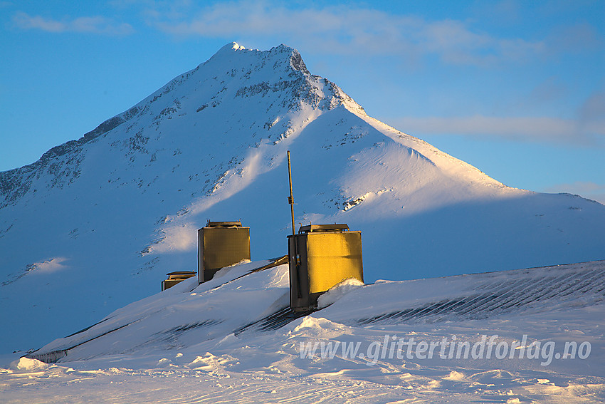 Taket på den nesten nedsnødde hovedhytte på Olavsbu med Snøholstinden (2141 moh) i bakgrunnen.